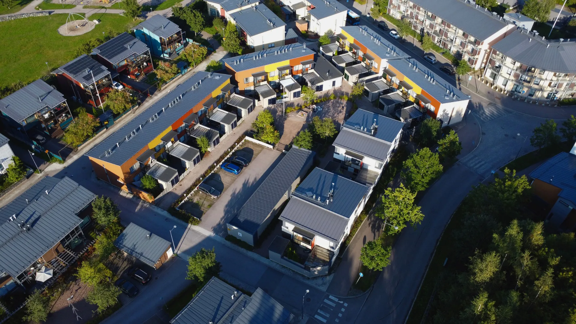 Ilmakuva modernista asuinalueesta, jossa rivitaloja ja pientaloja, aurinkoisessa säässä ja siellä täällä olevia puita.