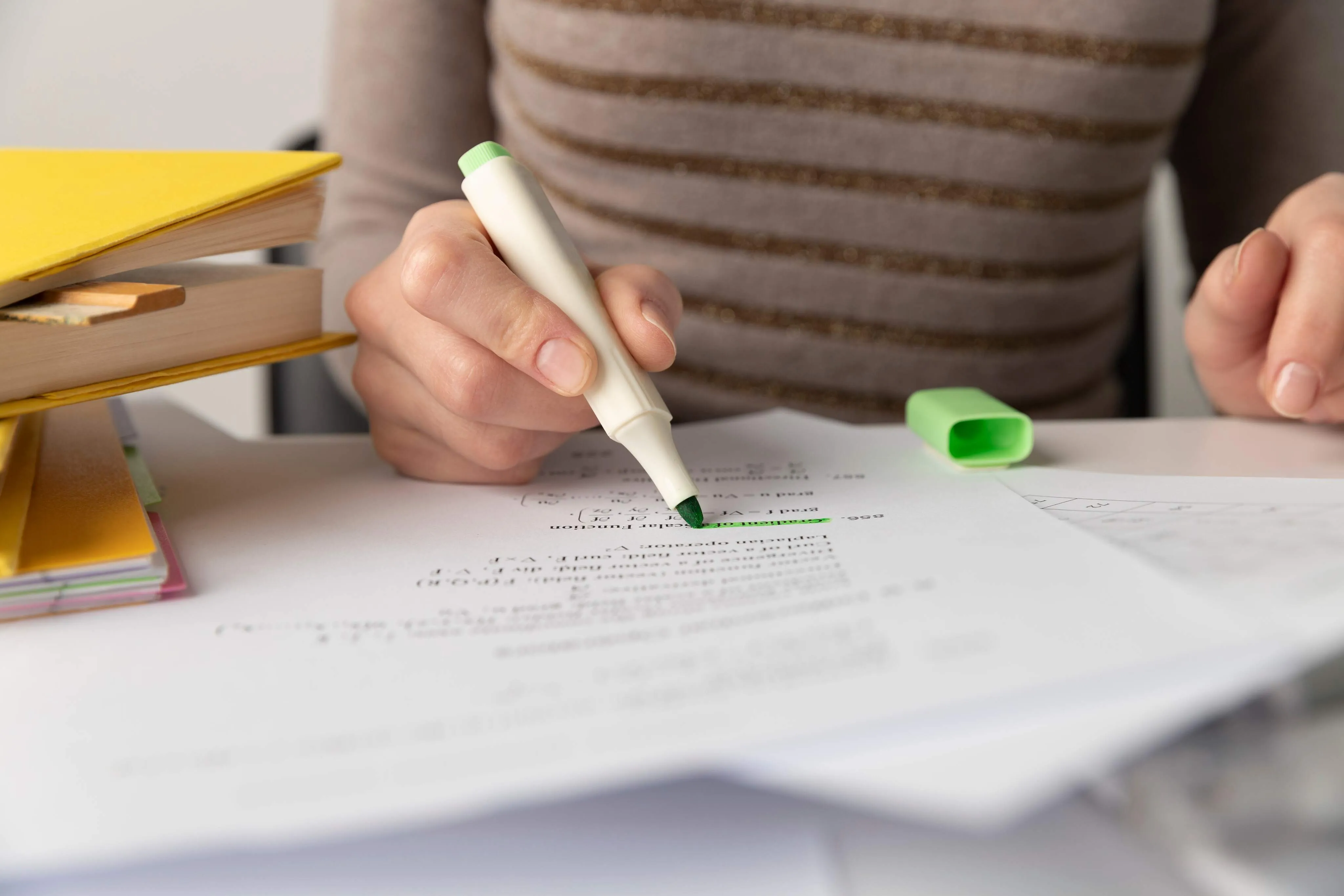 Persona subrayando texto con un marcador verde sobre una mesa con libros y papeles.
