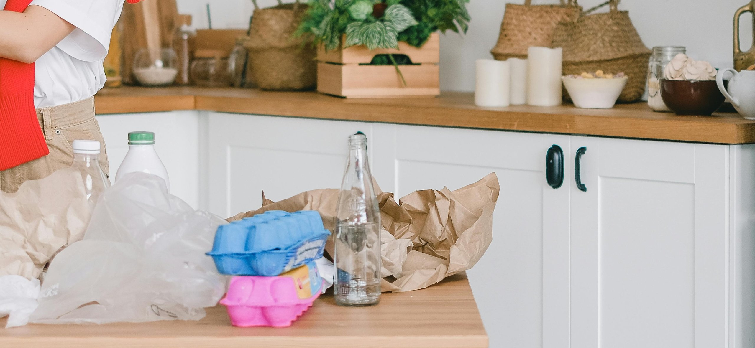 Person sorting recyclable items including plastic bottles, paper, and egg cartons on a kitchen counter.