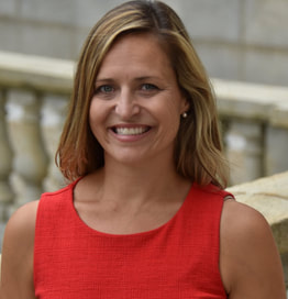 Smiling woman with blonde hair wearing a sleeveless red dress in an outdoor setting.