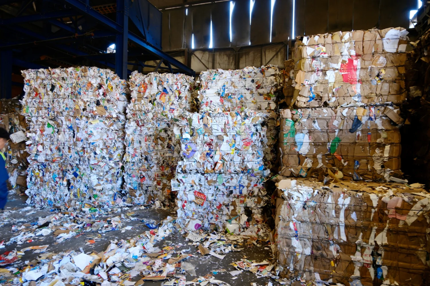 Large bales of compressed recyclable paper and cardboard stacked inside a recycling facility.