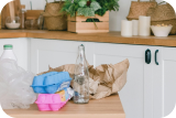 A kitchen countertop with plastic bottles, egg cartons, and brown paper bags ready for recycling.