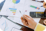 Person holding a pen above financial charts and graphs with a calculator on the table.