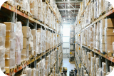 Warehouse aisle with tall shelves stacked with boxes and pallets on both sides.