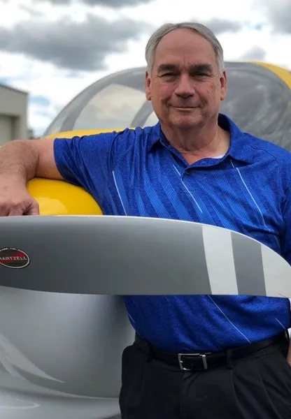 Man in blue shirt standing beside a small yellow airplane holding its propeller.