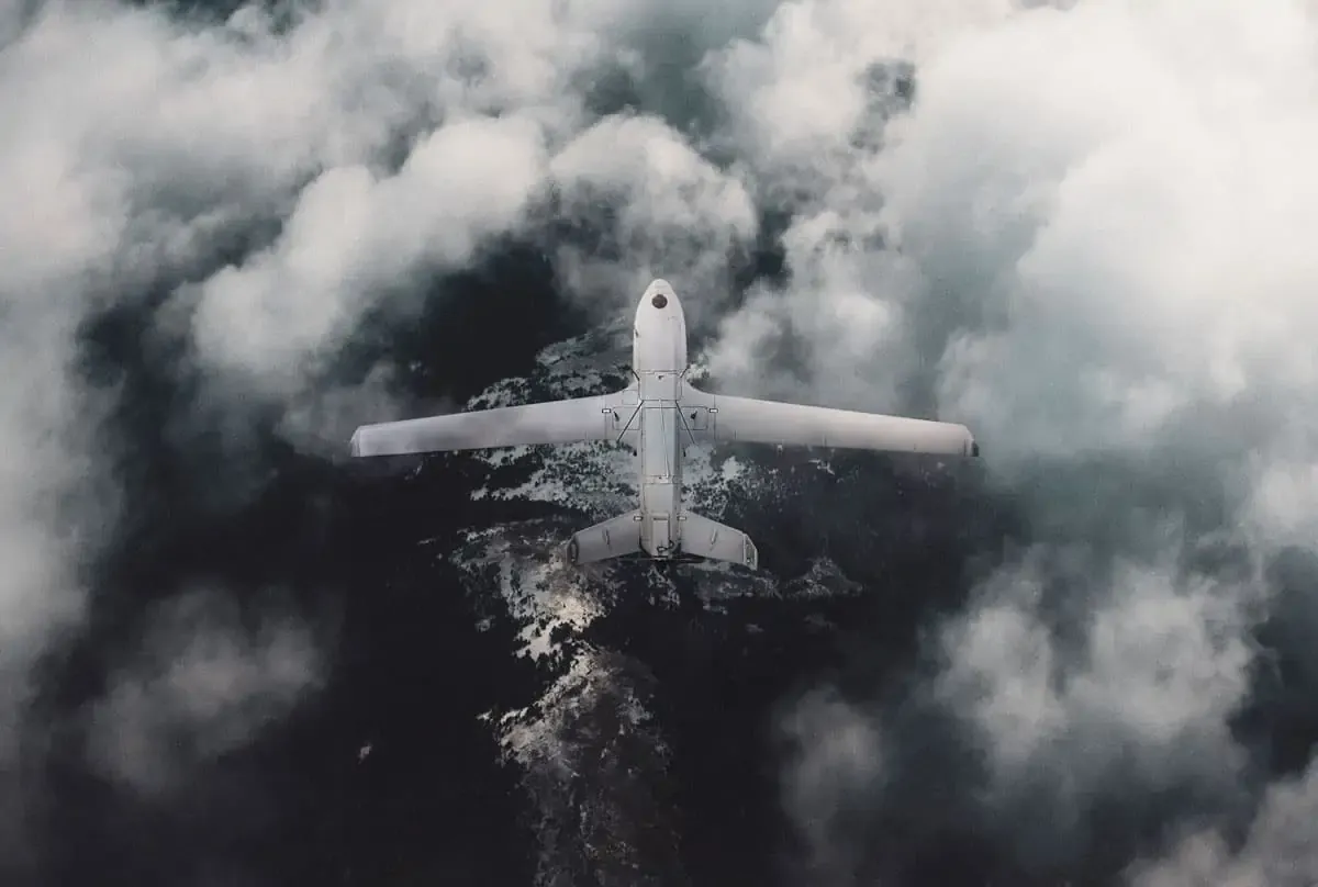 Aerial view of a white drone flying above dark water and surrounded by clouds.