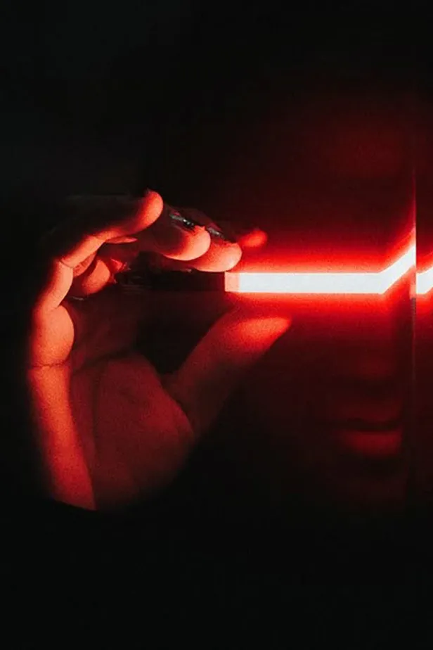 Hand holding a glowing red light strip in darkness, illuminating part of a face.