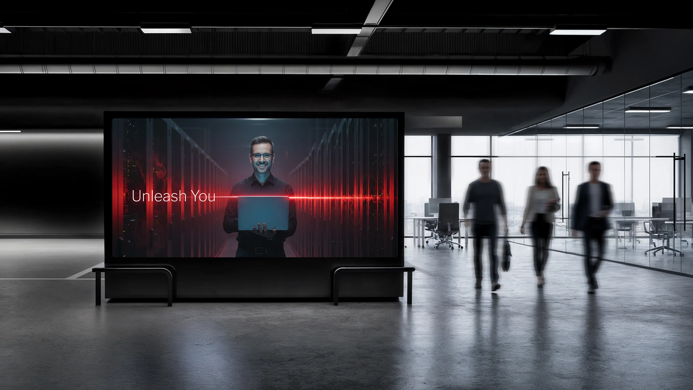 Digital billboard inside modern office shows a man holding a laptop with the text 'Unleash You' and red light effects, while three blurred people walk in the background.
