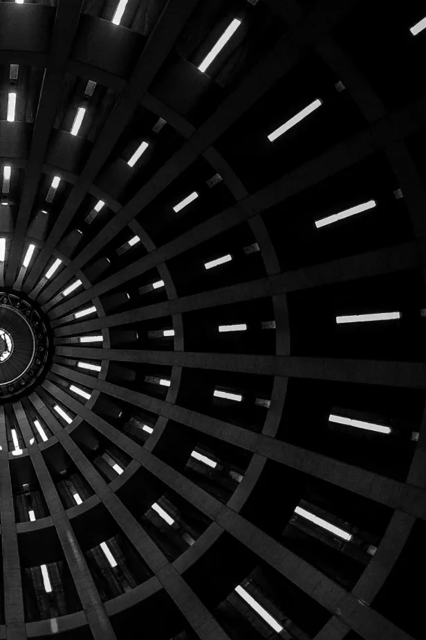Interior view looking up at a circular ceiling with evenly spaced vertical beams and rectangular light openings.