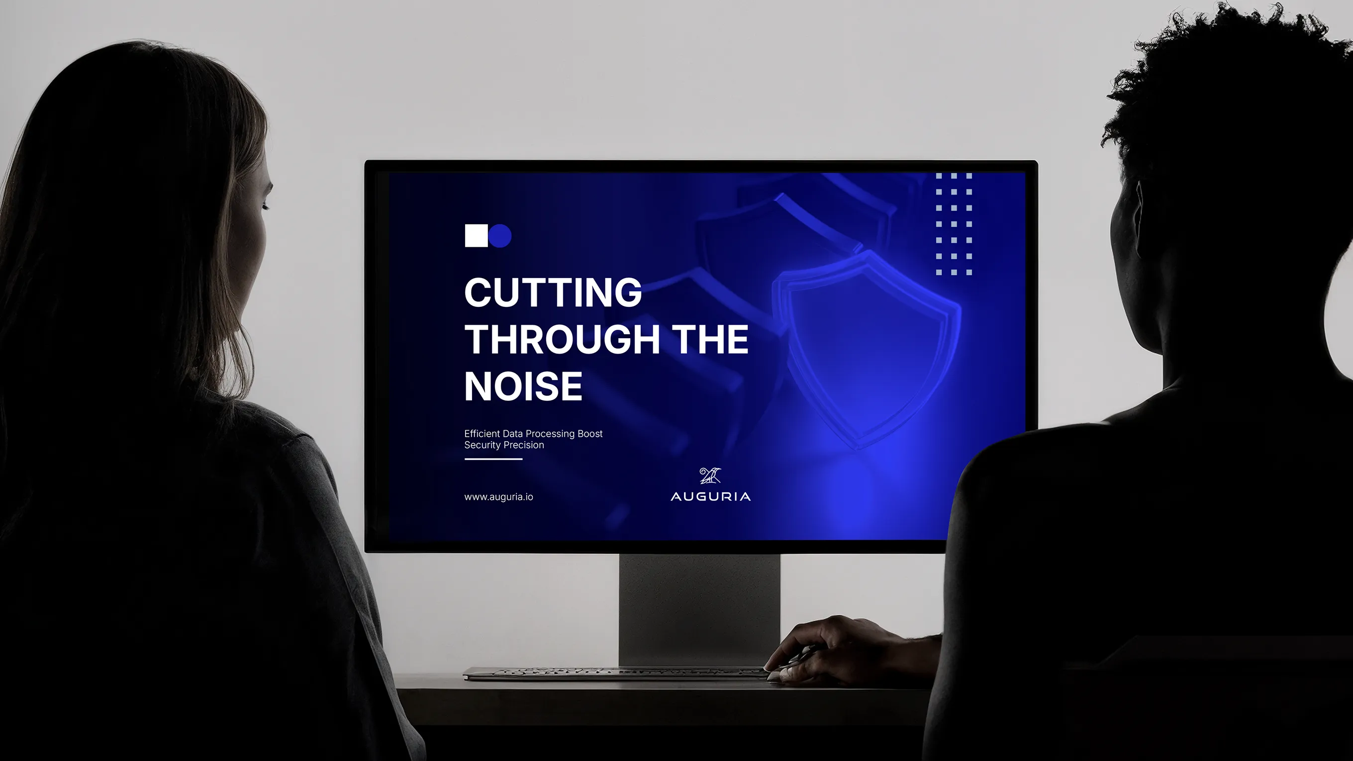 Two people sitting in front of a computer screen displaying the text 'Cutting Through the Noise' with a blue background and security shield icons.