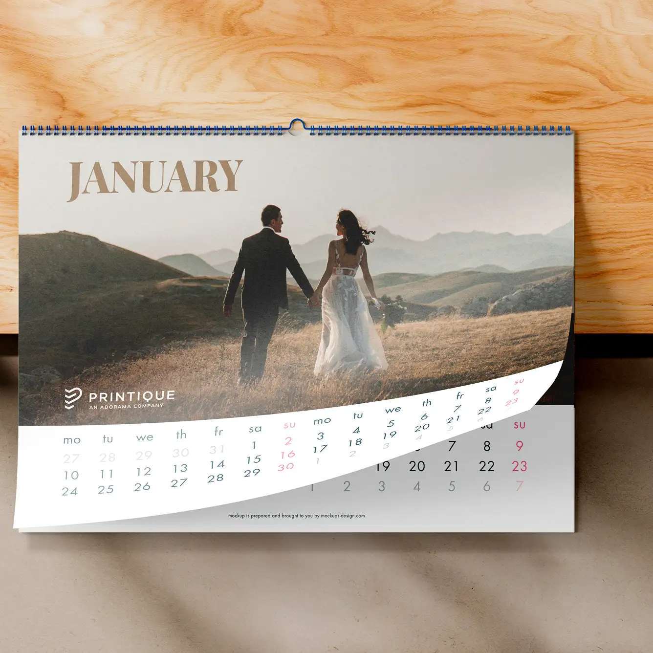 Wall calendar open to January page showing a couple holding hands walking in a grassy field with mountains in the background.