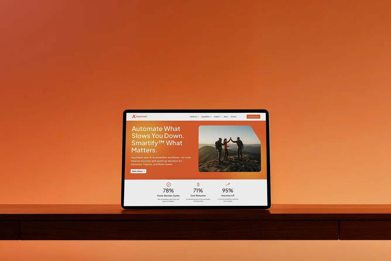 Tablet on wooden desk displaying Haystream website with orange theme, showing tagline, stats, and image of three hikers high-fiving.