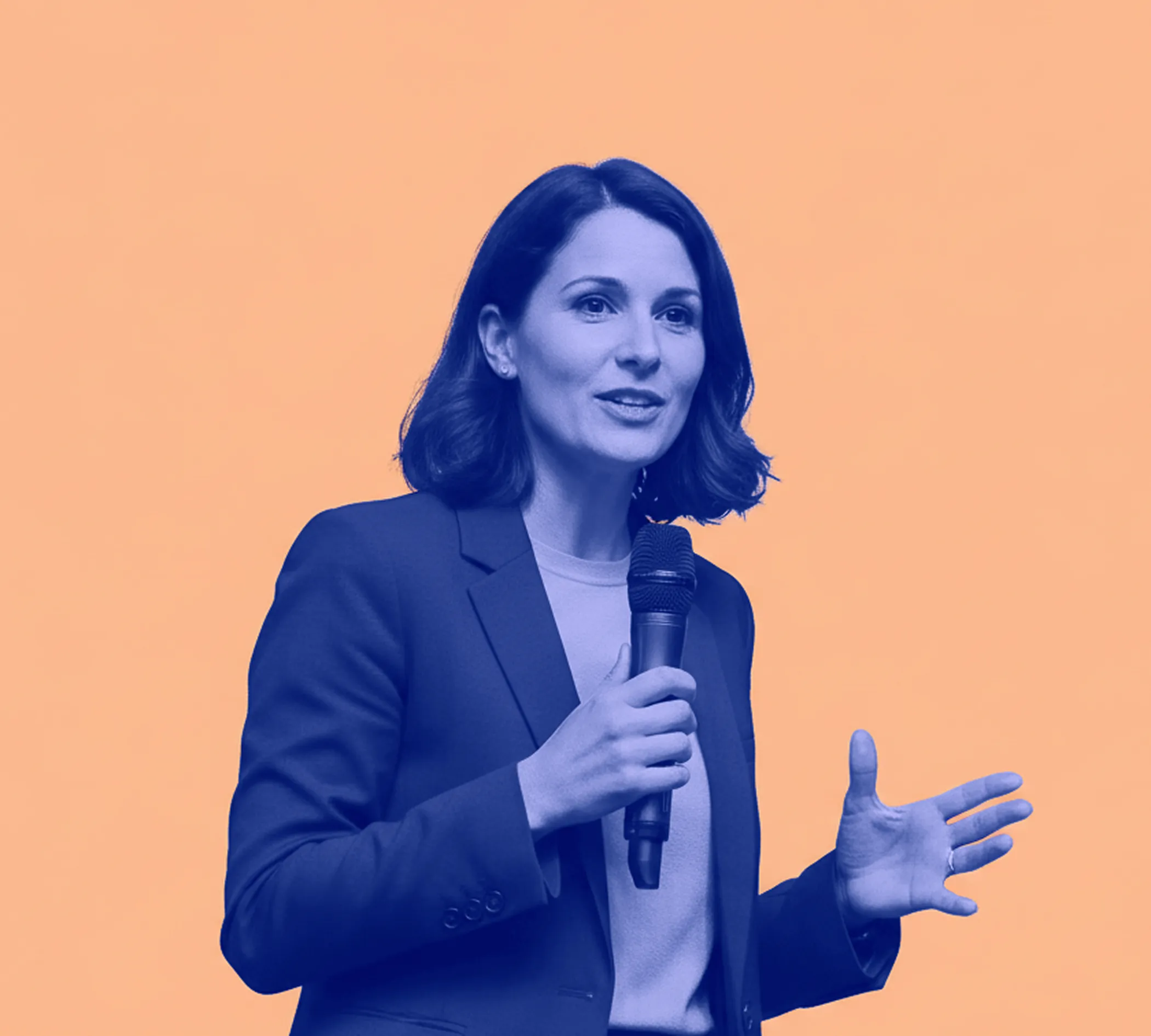 Woman in blazer speaking and holding a microphone against a solid peach background.