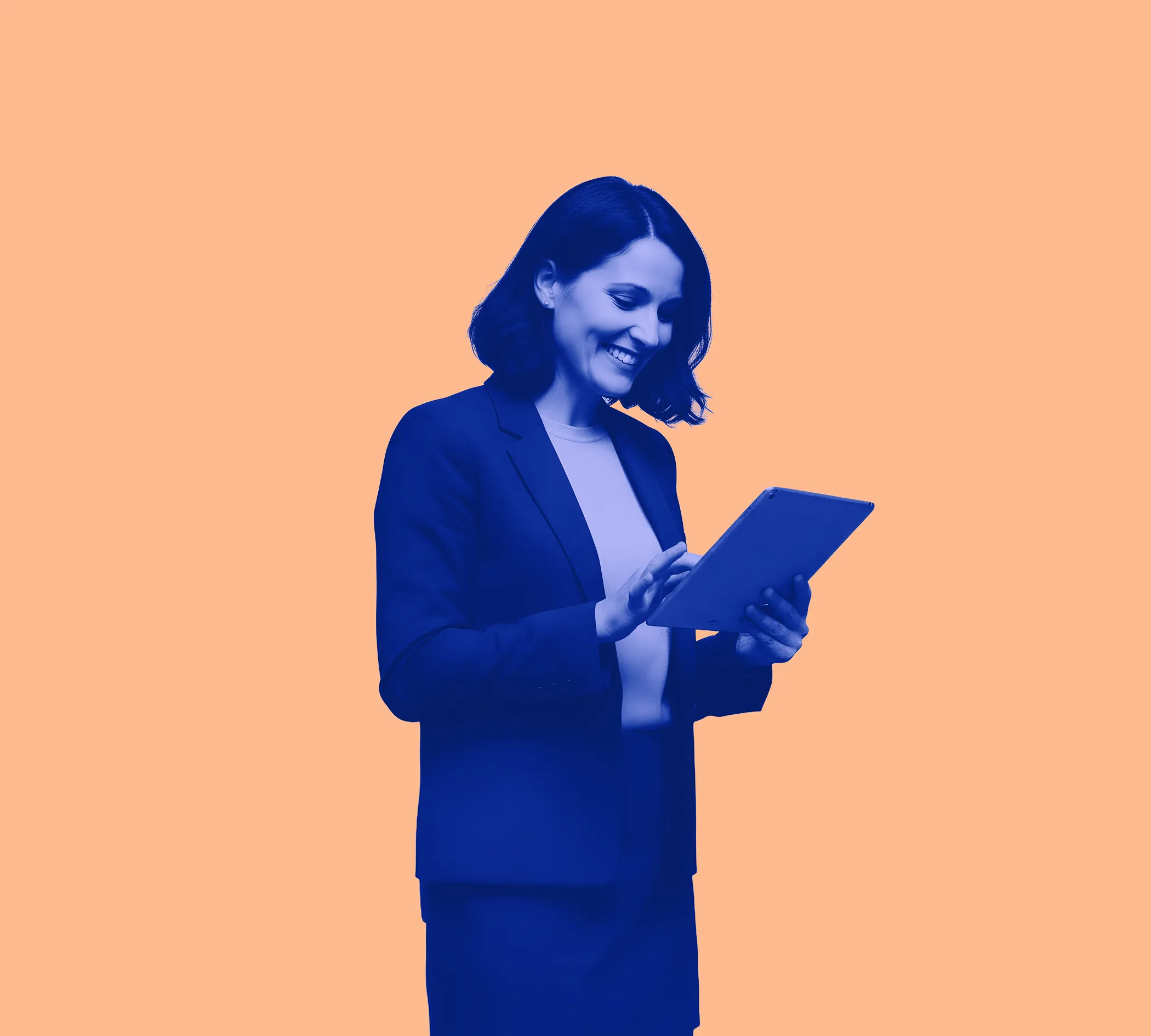 Smiling businesswoman in blazer using a tablet against a peach background.
