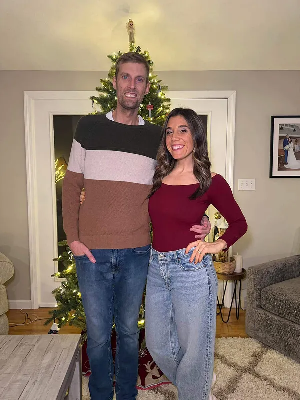 Katie Zarrilli and husband smiling in front of a decorated Christmas tree.