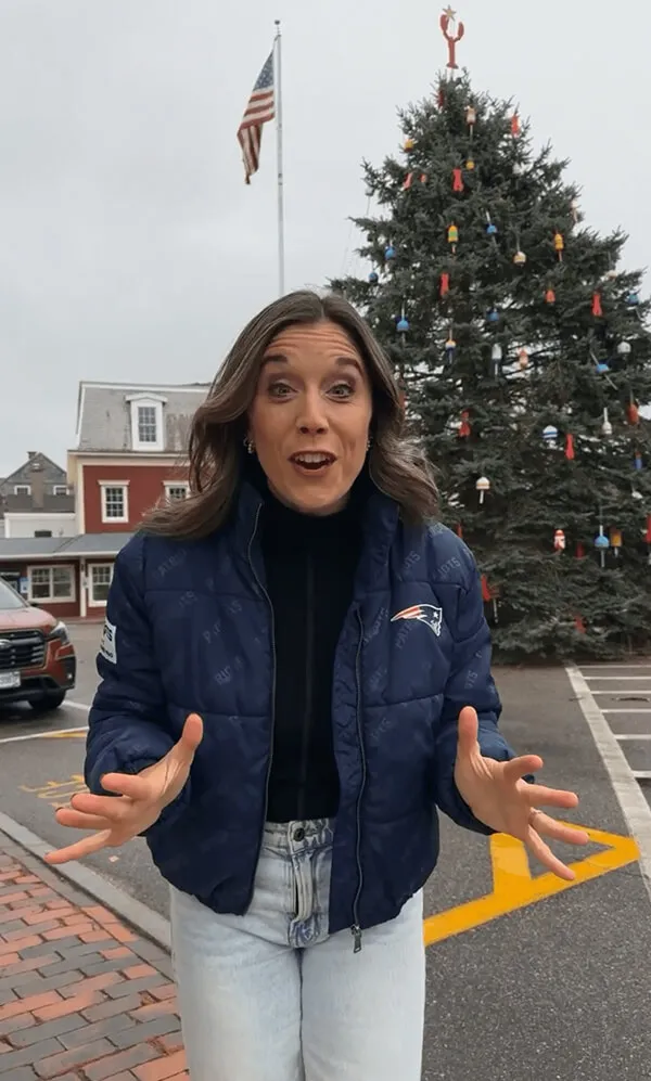 Katie Zarrilli in a Patriots jacket gesturing with hands, standing outdoors near a decorated Christmas tree.