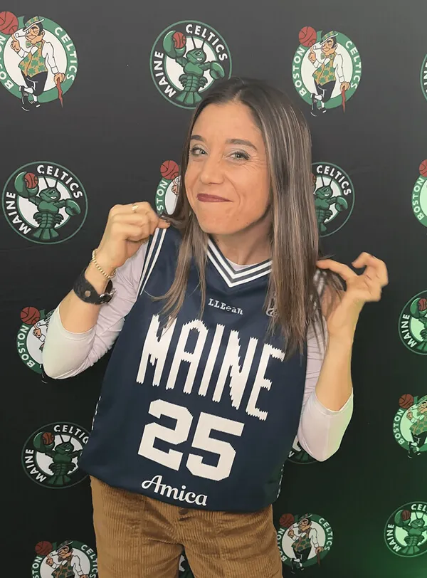 Katie Zarrilli holding a Maine 25 basketball jersey in front of a Boston Celtics backdrop.