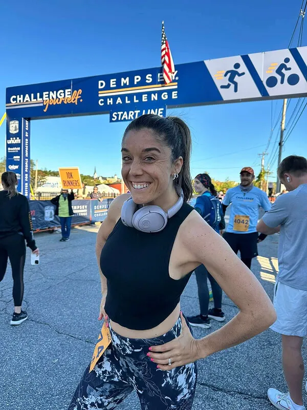 Katie Zarrilli wearing a black sleeveless top and floral leggings with headphones around her neck at the start line of the Dempsey Challenge race.