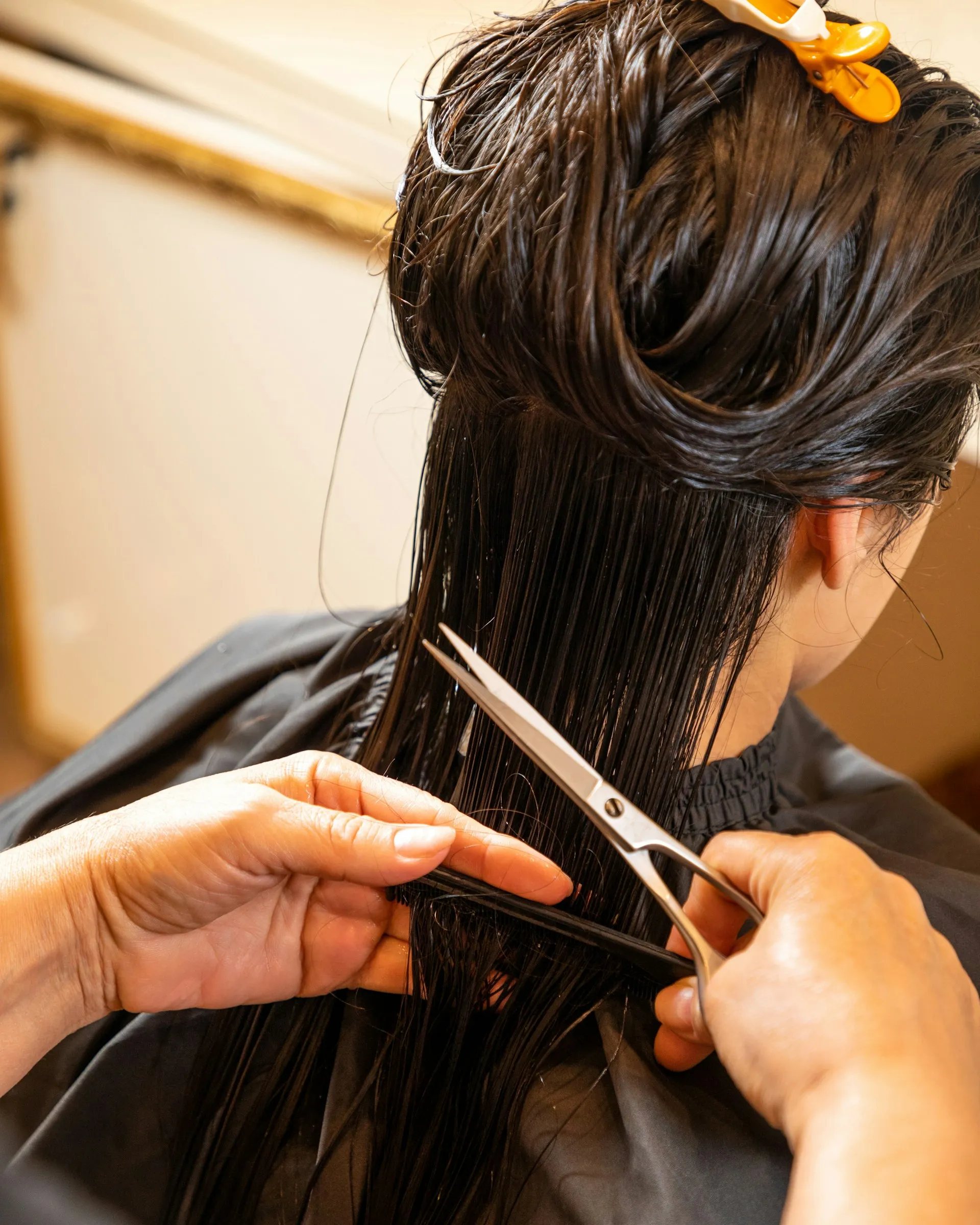 Close-up of hands cutting wet black hair with scissors at a salon.