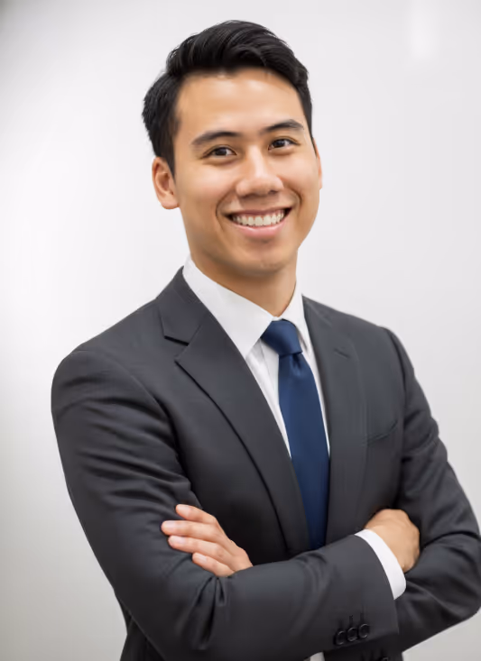 Nathaniel Lai in a dark gray suit and blue tie smiling with arms crossed against a plain light background.