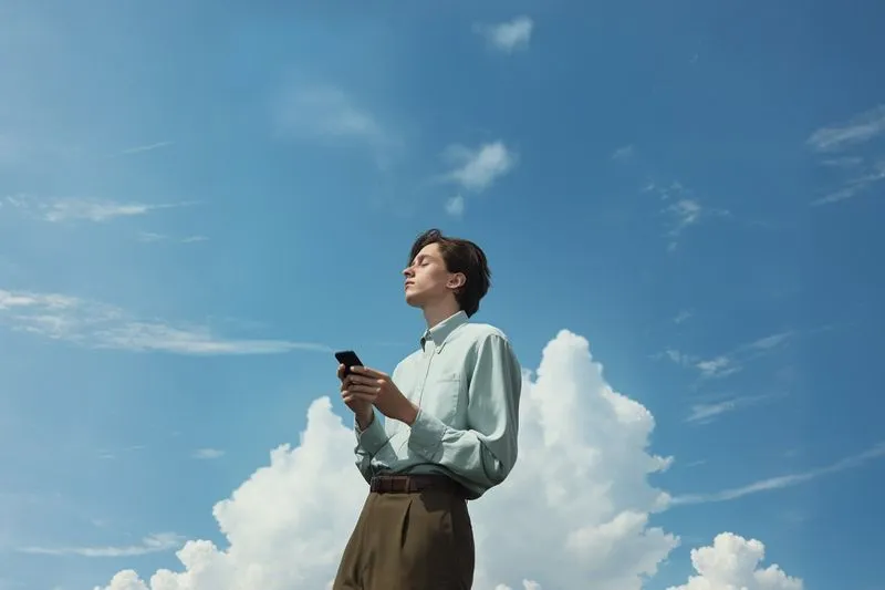 A man standing in front of a blue sky holding a cell phone.