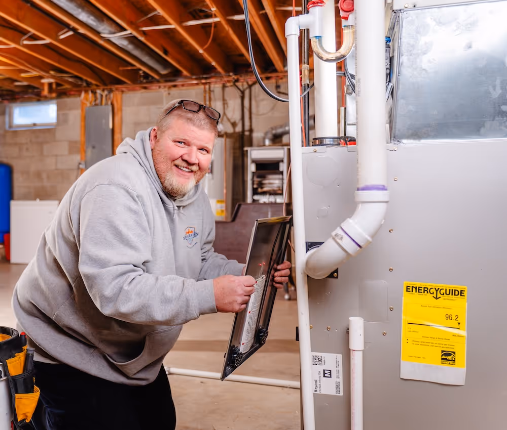 Smiling HVAC technician in a basement inspecting a furnace unit with an energy guide label, in canal winchester home