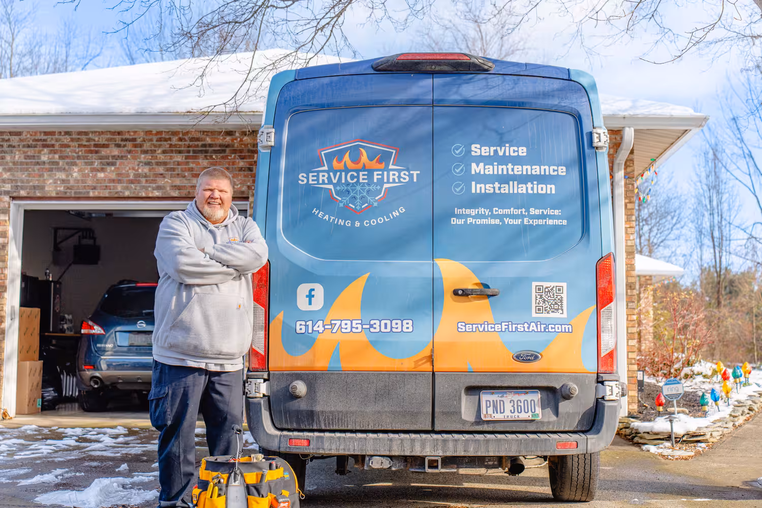 mini split technician standing with arms crossed next to a blue and orange heating and cooling service van with contact info and services listed.