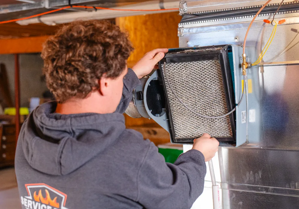 Technician replacing or inspecting an air filter in an HVAC system inside a basement in Groveport.
