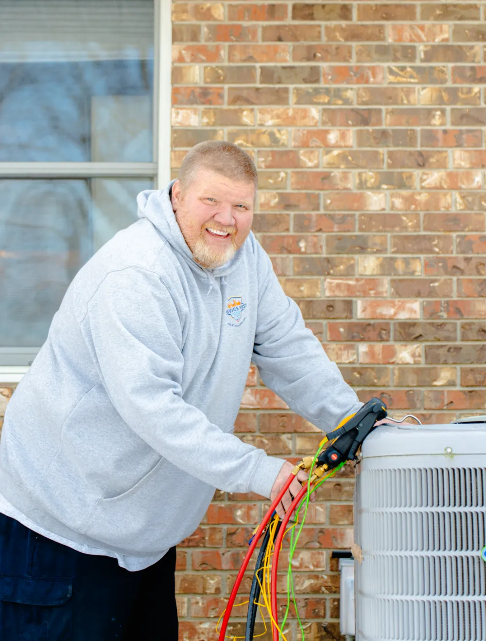 Technician in a gray hoodie working on an outdoor air conditioning unit with colorful diagnostic hoses in Reynoldsburg, Ohio.