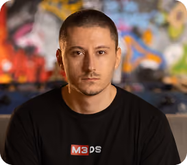 Portrait of a man with short hair wearing a black M3DS shirt against a colorful graffiti background.