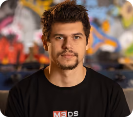 Portrait of a young man with short hair and beard wearing a black M3DS shirt.