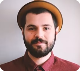 Man with beard and mustache wearing a brown hat and maroon buttoned shirt, smiling slightly.
