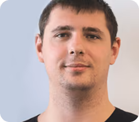 Close-up portrait of a man with short dark hair and light facial stubble wearing a black shirt.