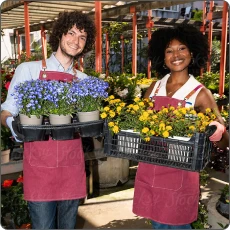 Deux fleuristes souriants, un homme tenant un plateau de pots de fleurs violettes et une femme portant une caisse de fleurs jaunes dans une serre.