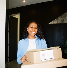 Une femme souriante tenant deux colis dans un intérieur moderne.
