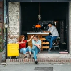 Trois personnes discutent dans un atelier avec des outils suspendus et une table de travail en arrière-plan.
