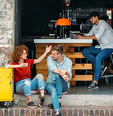 Trois personnes discutent dans un atelier avec des outils suspendus et une table de travail en arrière-plan.
