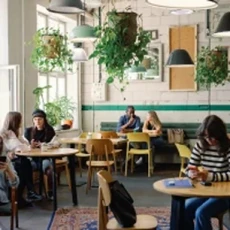Intérieur d'un café avec des clients assis aux tables et de nombreuses plantes suspendues au plafond.