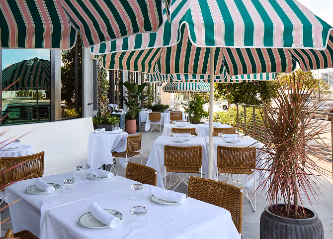 Elegant restaurant patio featuring white tablecloths, wicker chairs, and green and white striped umbrellas.