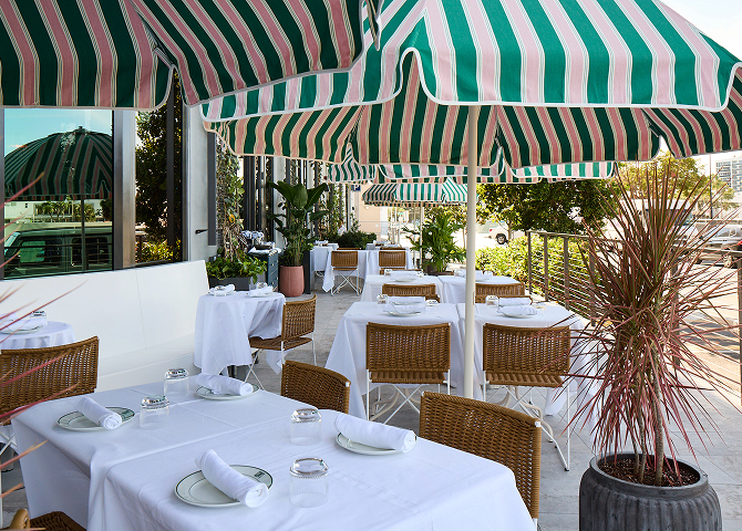 Elegant restaurant patio featuring white tablecloths, wicker chairs, and green and white striped umbrellas.
