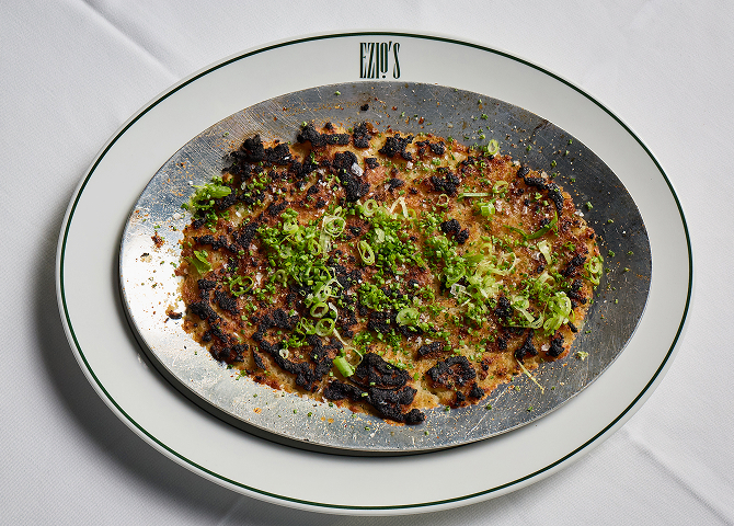 Gourmet grilled octopus with fresh herbs served on a metal and porcelain plate.