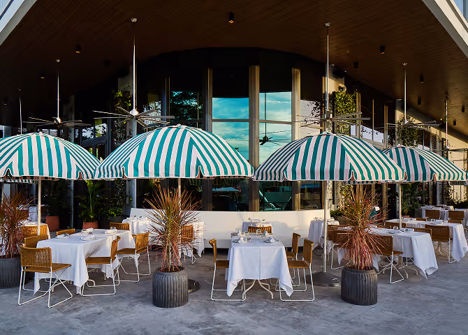 Elegant restaurant terrace with green and white striped umbrellas and tables set with white tablecloths.
