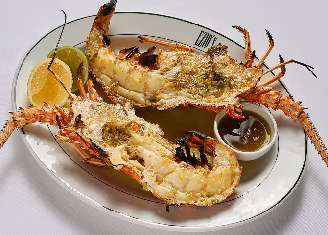 Gourmet grilled lobster dish with lemon wedges and dipping sauce.