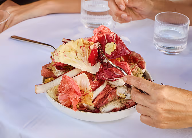 Red chicory and endive salad served in a white bowl on a restaurant table.