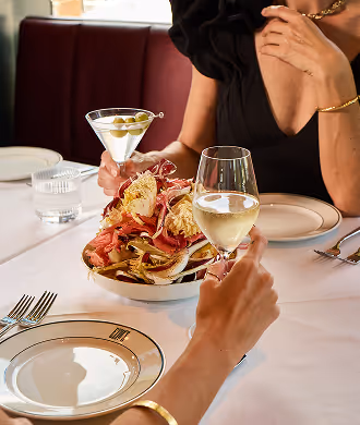 Two people sharing dinner with a Martini cocktail, a glass of white wine, and a plate of cured ham and focaccia.