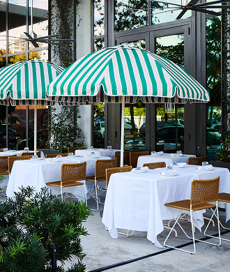 Elegant restaurant patio featuring white tablecloths and green and white striped umbrellas with fringe detailing.