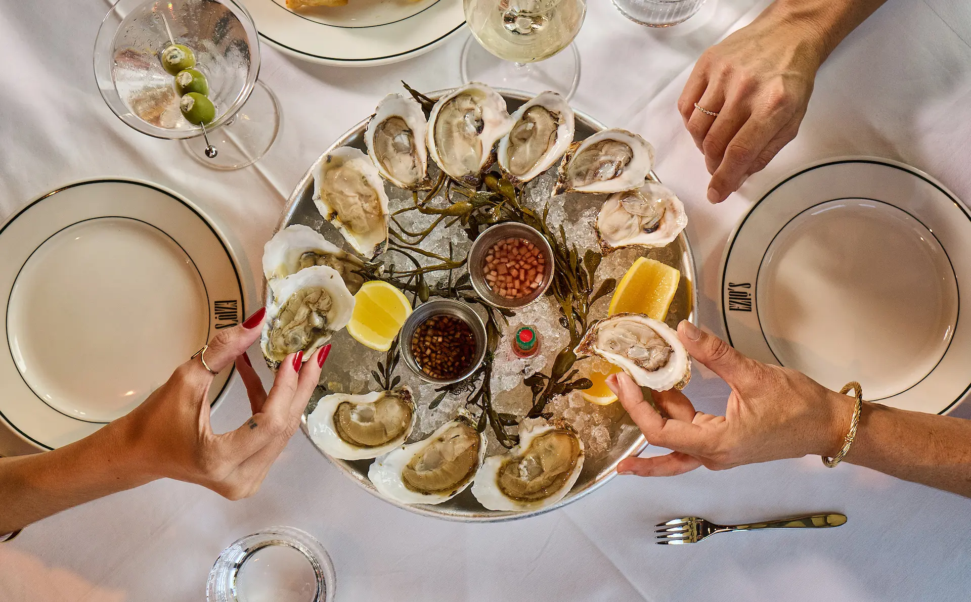 Fine dining restaurant interior featuring white tablecloths, dark chairs, and a large artistic purple chandelier hanging from the ceiling.
