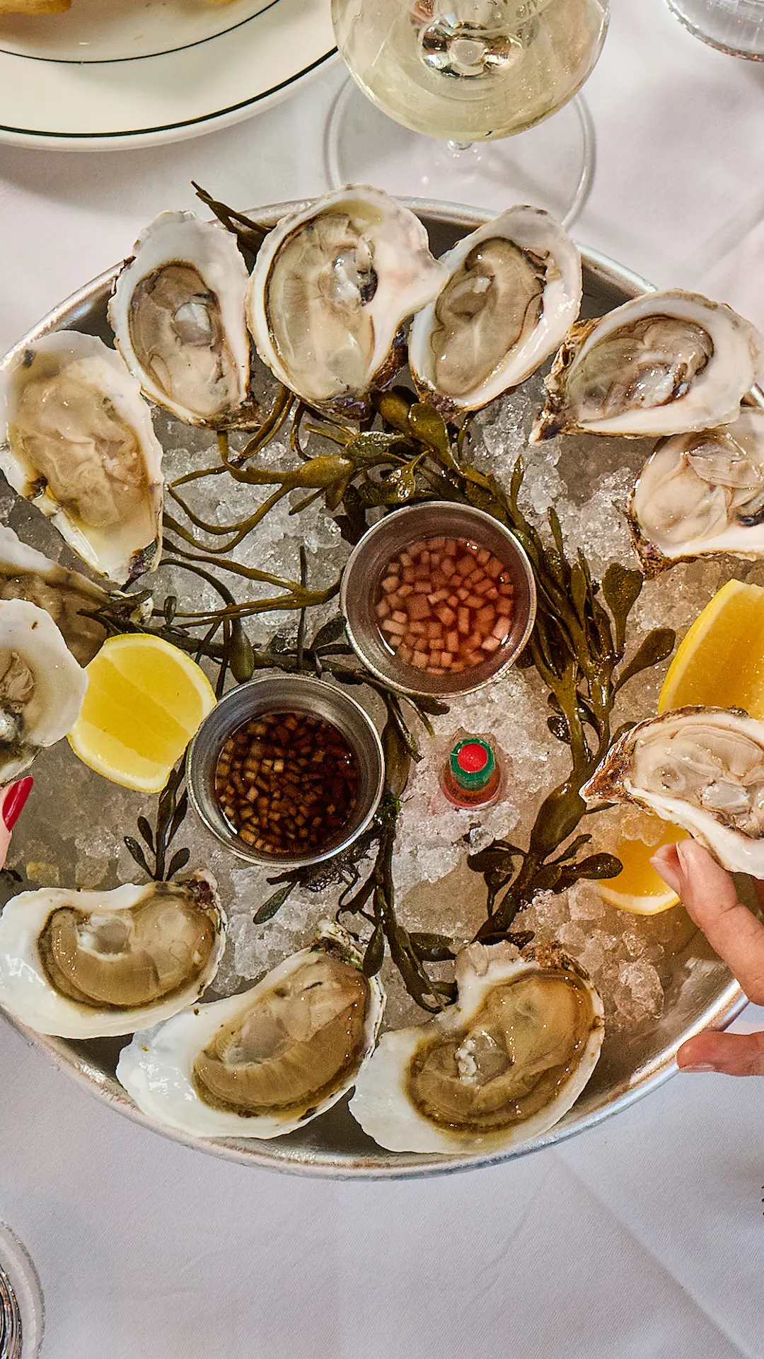 Fine dining restaurant interior featuring white tablecloths, dark chairs, and a large artistic purple chandelier hanging from the ceiling.