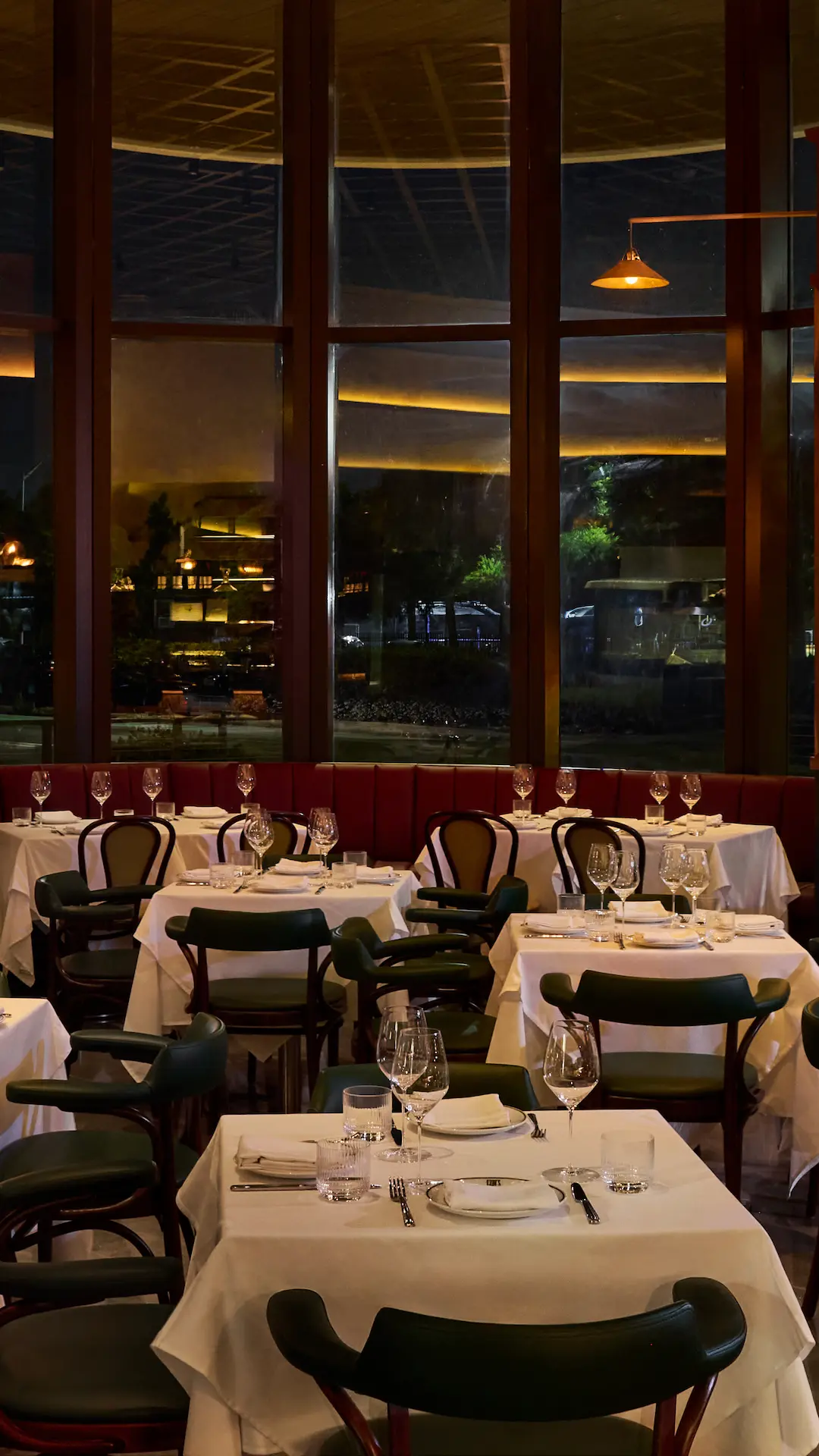 Fine dining restaurant interior featuring white tablecloths, dark chairs, and a large artistic purple chandelier hanging from the ceiling.