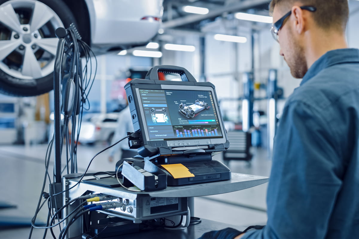 Technician using diagnostic equipment with car performance data displayed on a screen in a vehicle repair shop.